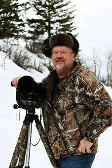 A man in camouflage holding a camera on top of a hill.