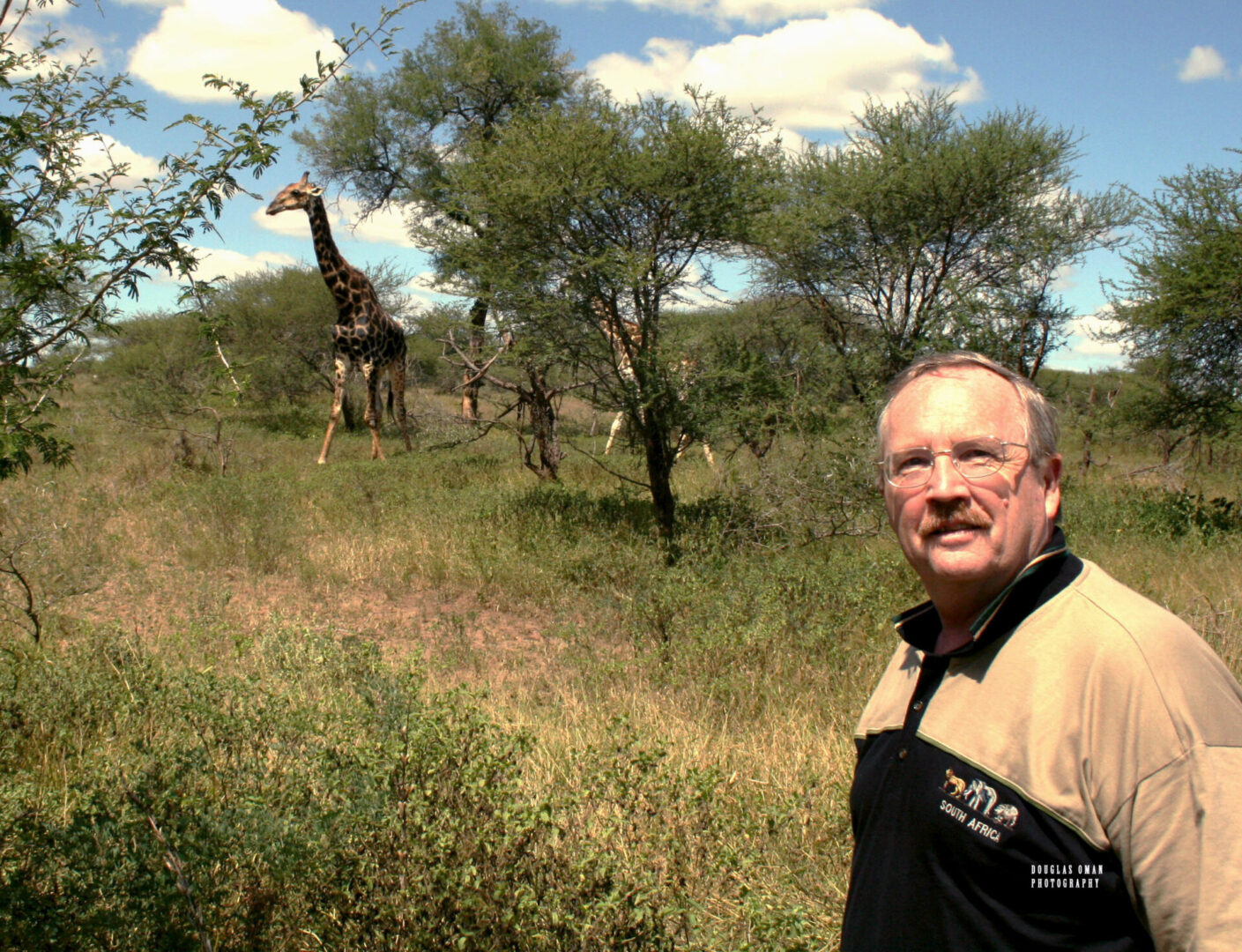 A man standing in front of some trees and giraffes